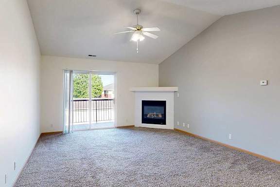 a carpeted living room with a vaulted ceiling, ceiling fan, gas fireplace, and sliding glass door to the balcony