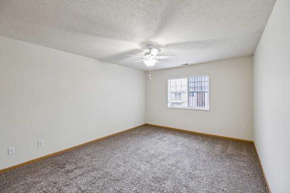 A room with a ceiling fan and a window with bars.