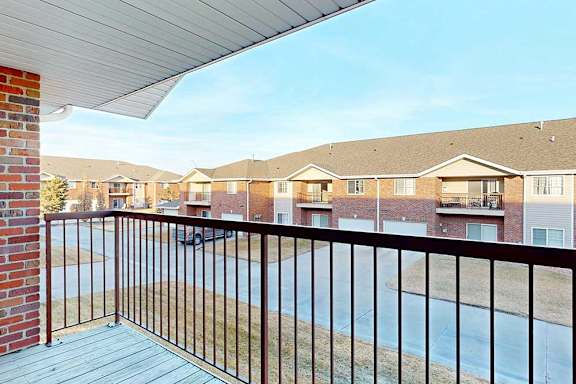 balcony with a black railing overlooks a street with houses on either side.