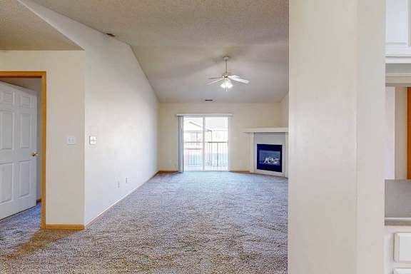 A spacious living room with a carpeted floor and a ceiling fan.