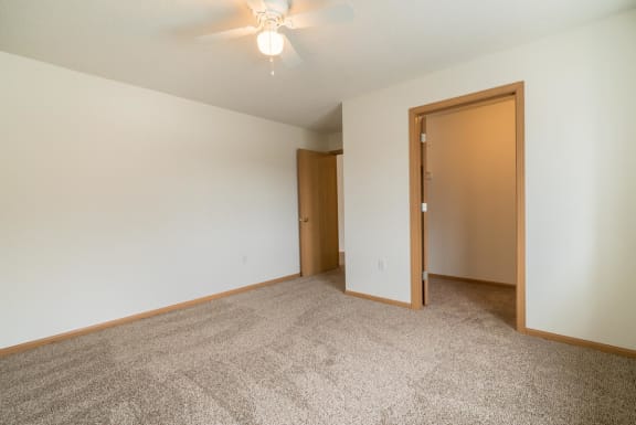 an empty bedroom with a ceiling fan and a door to a bedroom