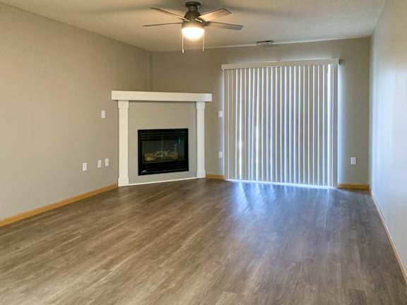 a living room with a fireplace and mantle, a ceiling fan, and vertical blinds
