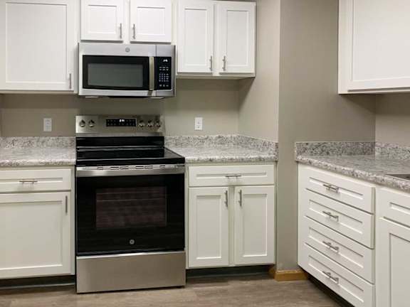 a kitchen with white cabinets, stainless steel appliances, and grey countertops
