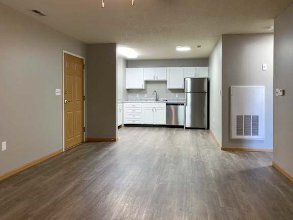 a living room with hardwood floors next to a kitchen with white cabinets and stainless steel appliances