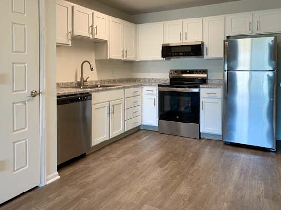 an updated L-shape kitchen with white cabinets, stainless steel appliances, granite countertops, and hardwood flooring