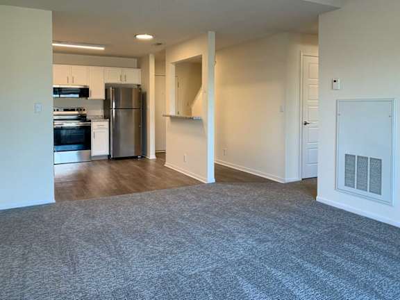 a living room the runs into a kitchen with hardwood floors, stainless steel appliances and white cabients