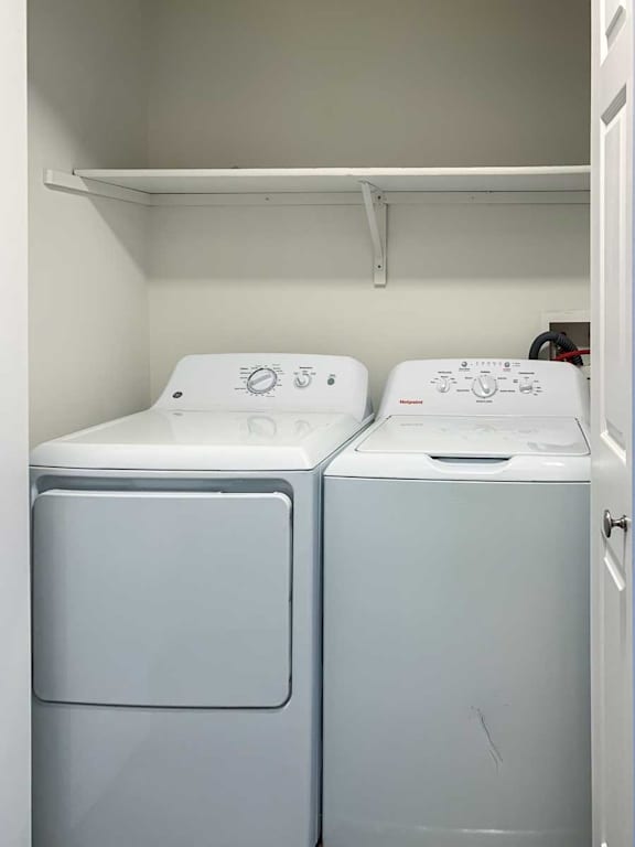 a laundry closet with side-by-side full-sized washer and dryer with overhead shelving