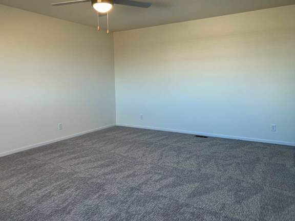 a spacious bedroom with carpeted flooring and a ceiling fan