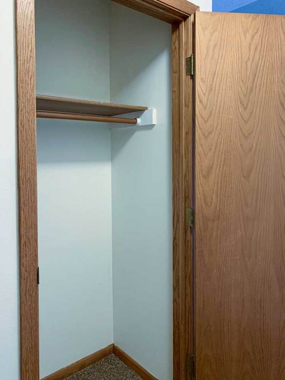 a hallway coat closet with a built-in shelf and a wooden door