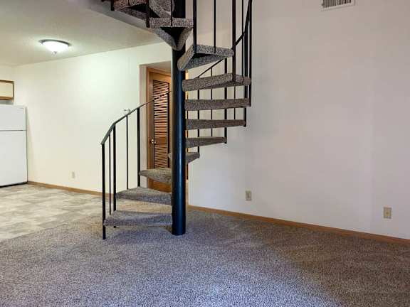 a spiral staircase with a metal railing and a carpeted floor in a living room