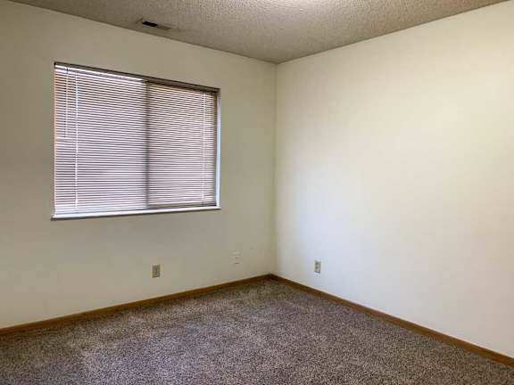 a bedroom with white walls, carpeted flooring, and a window with blinds