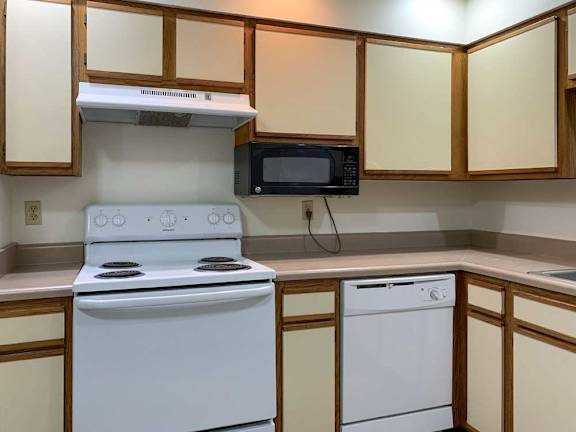 a kitchen with a white stove and dishwasher, a mounted microwave, and white and wooden cabinets