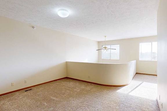 A carpeted loft bedroom with a view open to below, two bright windows, and a ceiling fan.