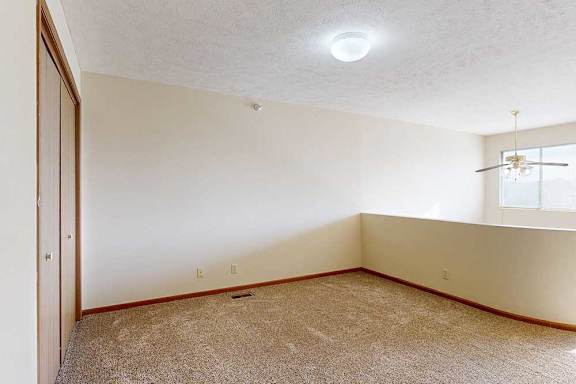 A carpeted loft bedroom with a view open to below, two bright windows, a sliding double-door closet, and ceiling fan.