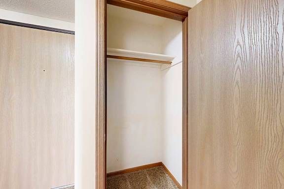 A coat closet with a built-in overhead shelf and hanging bar.