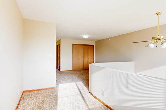 A carpeted loft bedroom with a view open to below, a sliding double-door closet, and a ceiling fan.