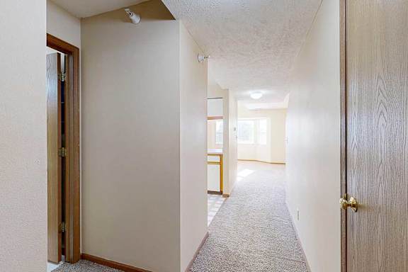 An entryway with an alcove to the left featuring a coat closet and the hallway half-bath, and a hall leading to the kitchen and living room.