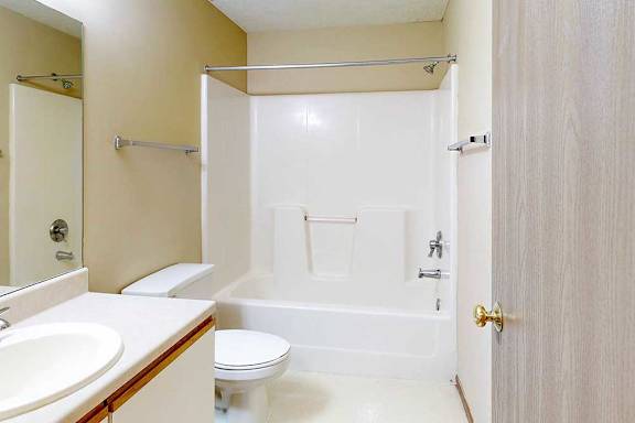 A bathroom with a white and oak vanity sink, tall mirror, towel rack, and combination shower and tub.