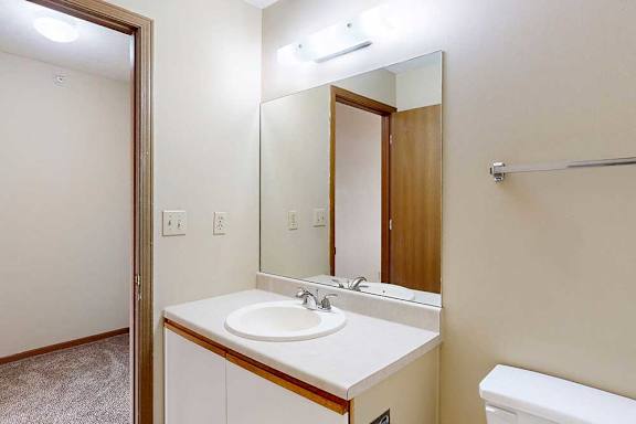 A bathroom with a white and oak vanity sink, tall mirror, towel rack.