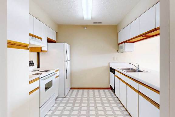 A galley kitchen with white cabinets with oak trim, white appliances, a double-basin sink, and a pass-through window countertop.