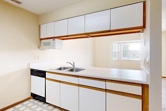 A galley kitchen with white cabinets with oak trim, white appliances, a double-basin sink, and a pass-through window countertop.