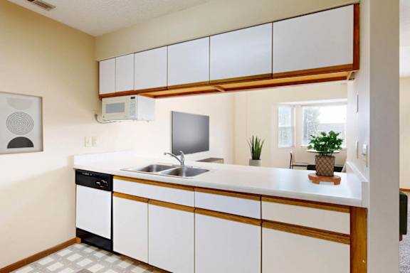 A kitchen with a white counter, white cabinets, and a pass through to the living room.