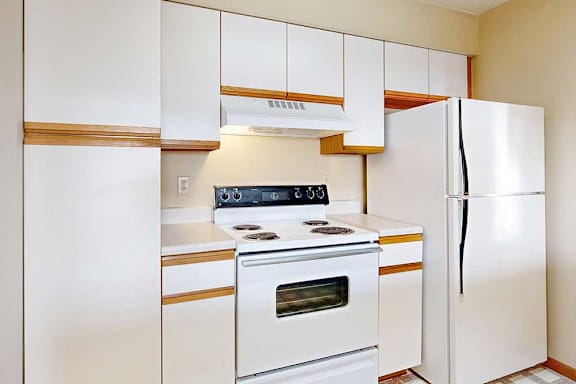 A galley kitchen with white cabinets with oak trim, and white appliances.