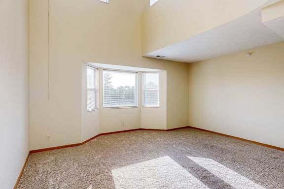 A carpeted living room with a bay window, and a two-story ceiling above.