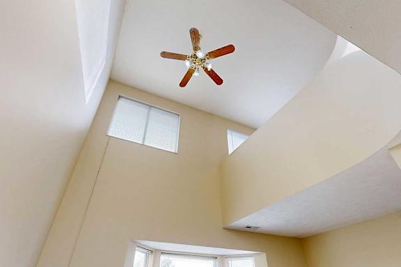 A carpeted living room with a bay window, and a two-story ceiling above.