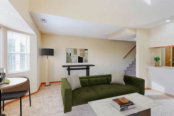 A living room with a green couch, a coffee table, and a staircase in the background.