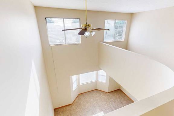 A carpeted loft bedroom with a view open to below, two bright windows, and a ceiling fan.