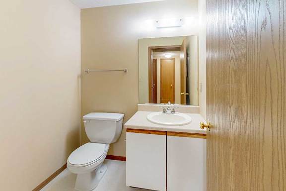 A hallway half bathroom with a white and oak vanity sink, tall mirror, and towel rack.