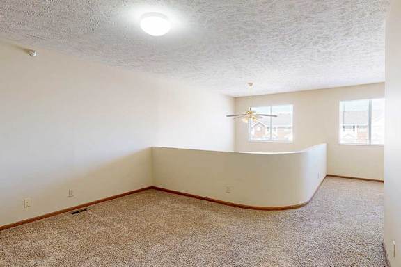 A loft bedroom with two windows, a ceiling fan, and a opening to the living room below.