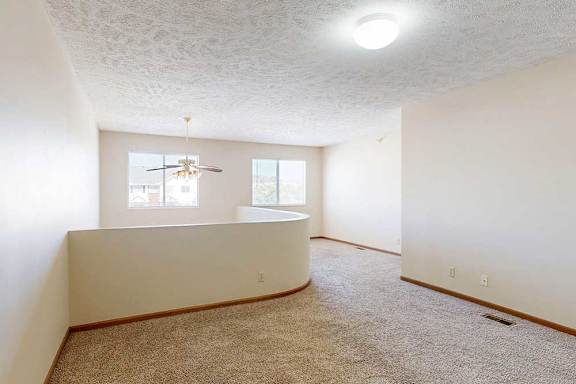 A loft bedroom with two windows, a ceiling fan, and a opening to the living room below.