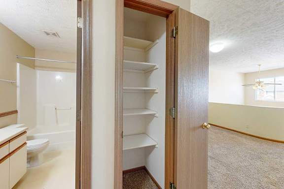 A linen closet with built-in shelves, next to an open door to the bathroom.