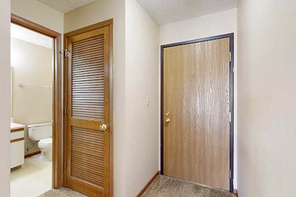 A front door next to an open door to a hallway bathroom.