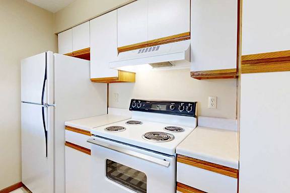 A galley kitchen featuring white cabinets with oak trim and white appliances.