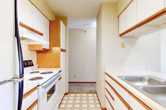 A galley kitchen featuring white cabinets with oak trim, white appliances, and a passthrough countertop to living room.