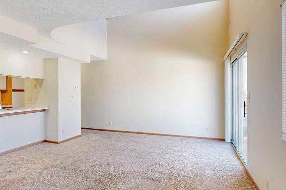 A carpeted living room with access to the kitchen via a pass-through window countertop, and a staircase to the upper loft area.