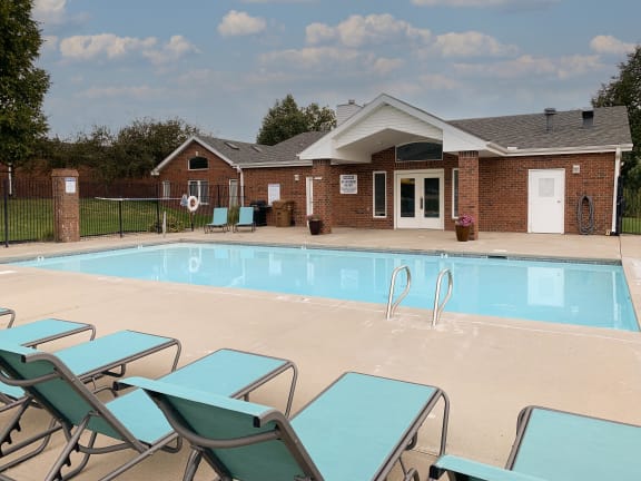 a swimming pool with blue chaise lounge chairs and the clubhouse in the background