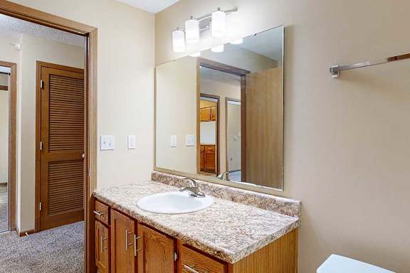 A bathroom with a vanity sink, mirror with overhead lighting, and wooden cabinet.