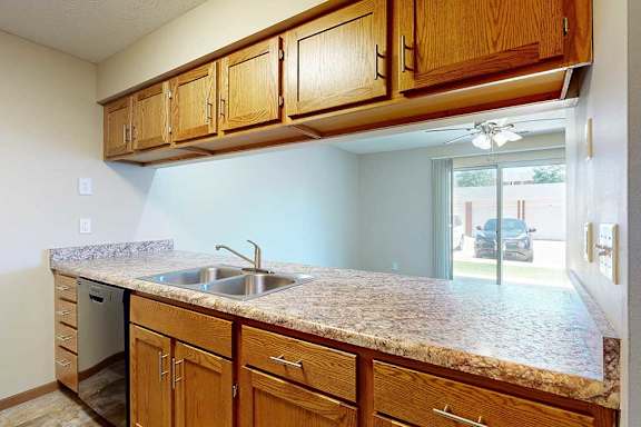 A kitchen with wooden cabinets, granite countertops, a double basin sink, and a view of the living room through a passthrough countertop.