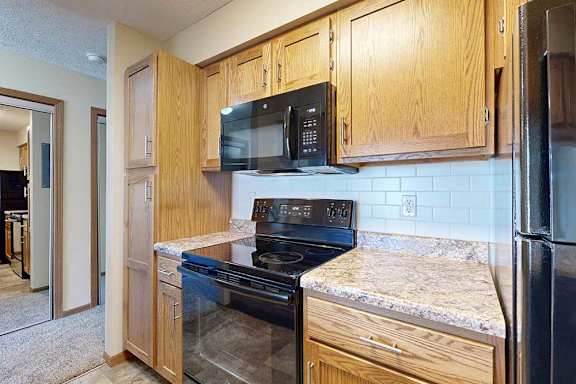 A galley kitchen with wooden cabinets, black appliances, and a tile backsplash.