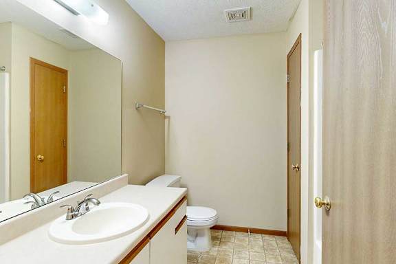 A bathroom with white and oak cabinetry, a wide vanity sink, and a large mirror with overhead lighting.