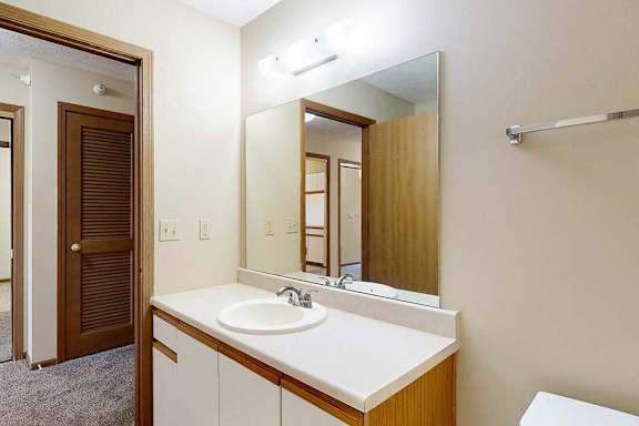 A bathroom with white and oak cabinetry, a wide vanity sink, and a large mirror with overhead lighting.
