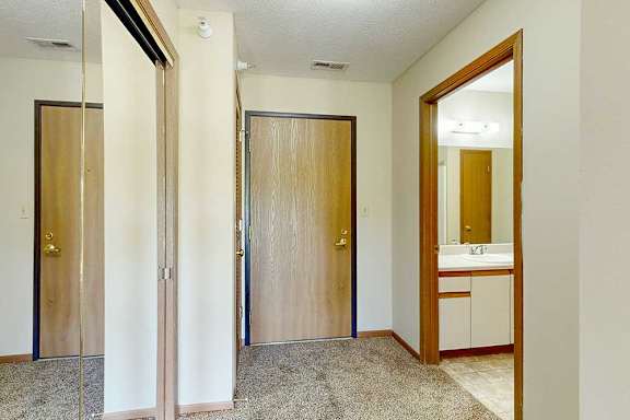 A wooden front door in a hallway that connects with a bathroom.