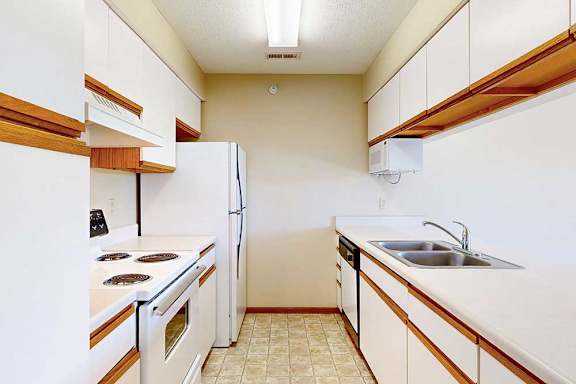 A galley kitchen featuring white cabinets with oak trim, white appliances, and a passthrough countertop window.