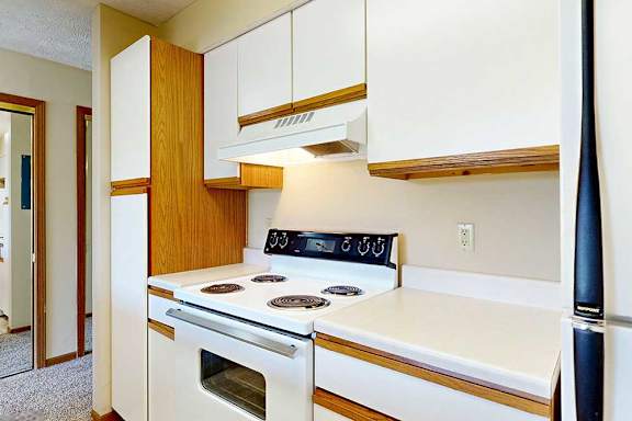 A galley kitchen featuring white cabinets with oak trim and a white stove.