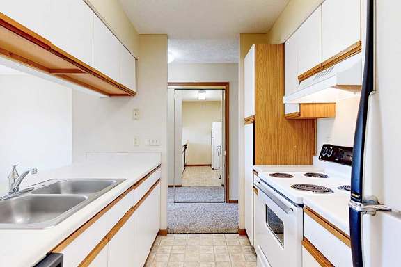 A galley kitchen featuring white cabinets with oak trim, white appliances, and a passthrough countertop window.