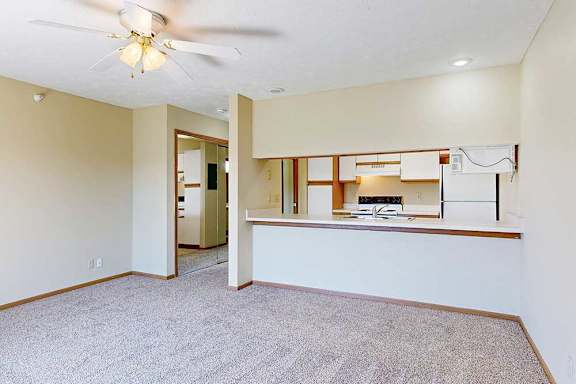 A living area with a ceiling fan and a view of the kitchen with white and oak cabinets.